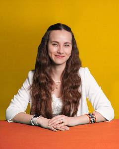 Headshot of Ingrid Gonzalez yellow background orange table.