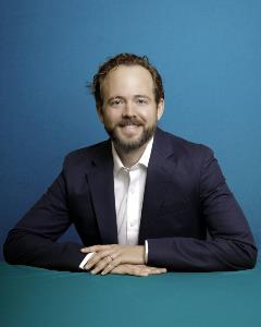 Headshot of Justin Reed on blue background