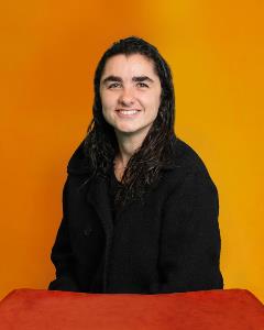 Headshot of Ana Maria Molina orange background red table.